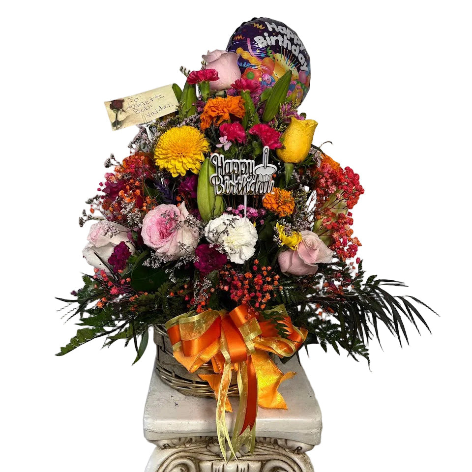 Mixed flower birthday arrangement in woven basket with colorful accents and happy birthday topper