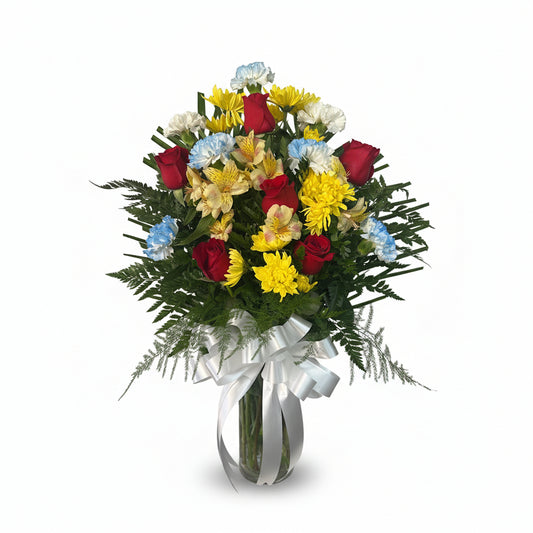 Colorful floral vase arrangement with red roses yellow mums blue carnations and fresh greenery by Houston florist